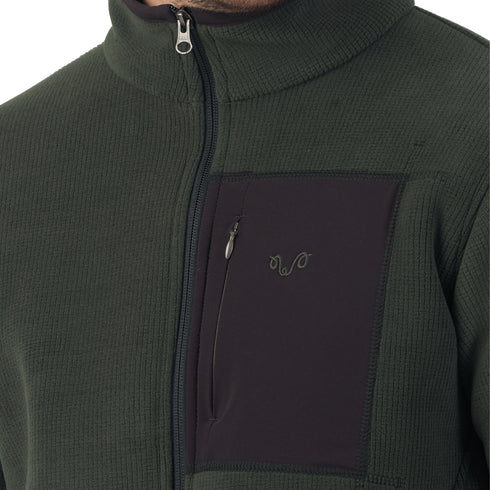 Mann mit Übergangsjacke aus Merinowolle im Innenbereich in der Farbe grün mit Brusttasche in schwarz.