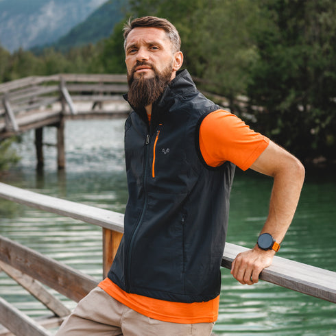 Mann lehnt sich gegen ein Geländer vor einem Fluss auf einer Brücke und trägt eine Laufweste mit Merinowolle.